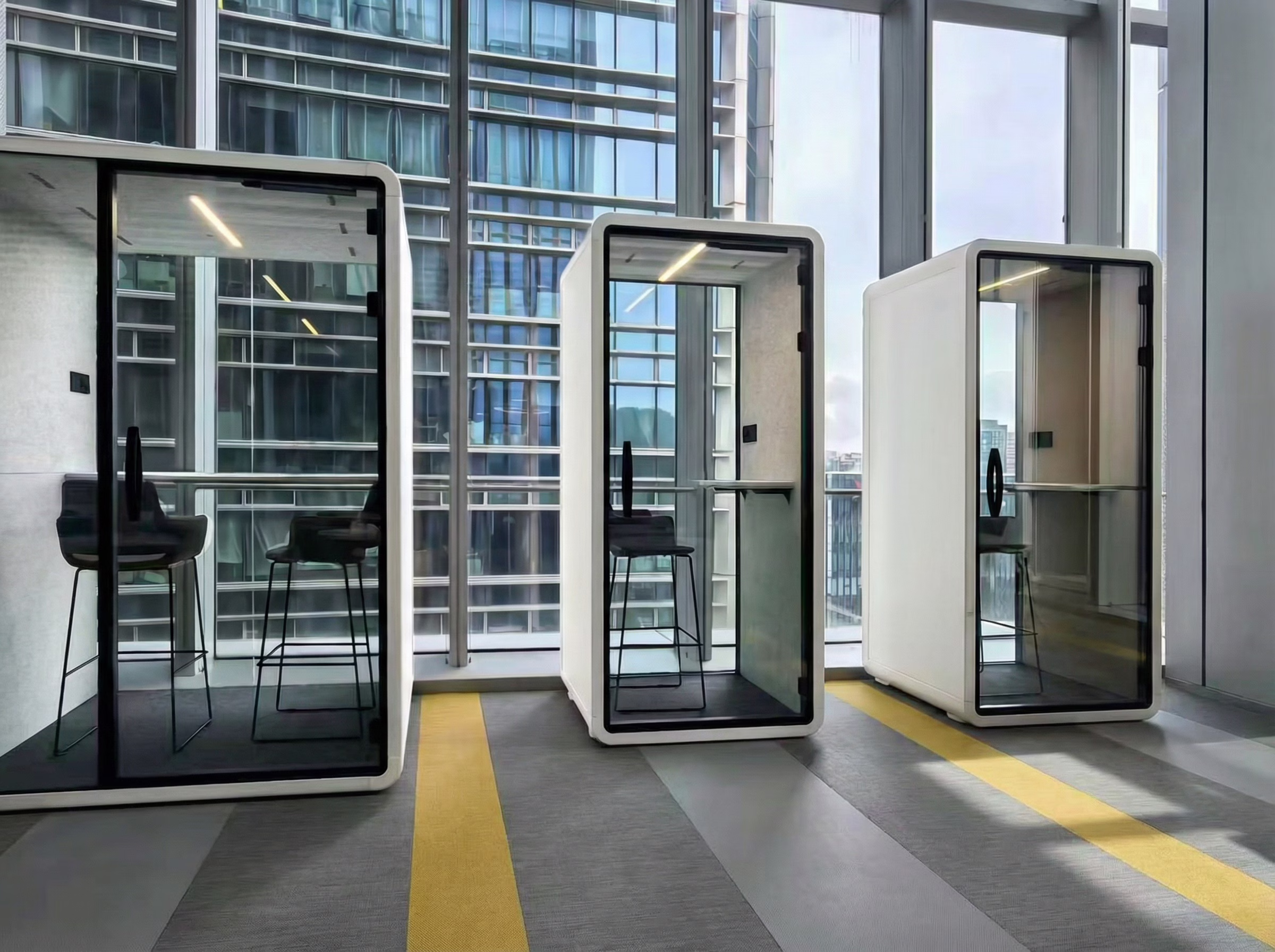 Three modern soundproof acoustic phone booths with glass doors in a bright office environment.